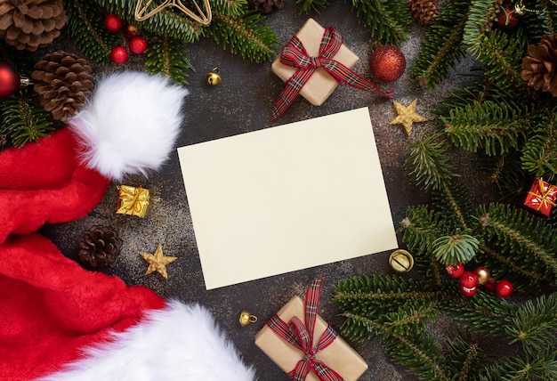Cartão de papel entre decorações de Natal, caixas de presente de chapéu de Papai Noel e ramos de abeto verde