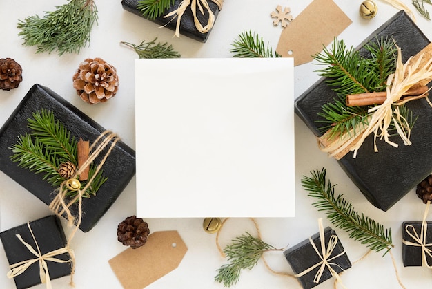 Cartão de papel entre decorações de Natal caixas de presentes pretas e ramos de abeto verde vista de cima