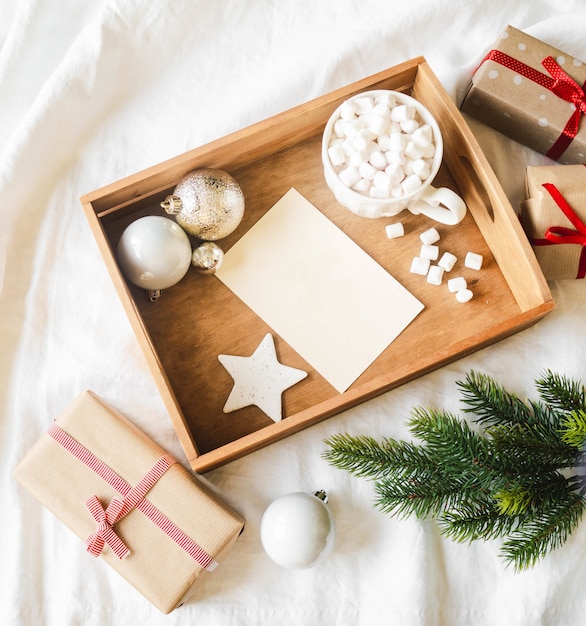 Cartão de papel por carta na bandeja de madeira, caneca com bebida quente e marshmallows e decoração de Natal. Postura plana para feliz Natal ou feliz ano novo.