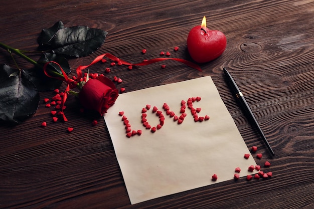 Cartão de presente para o dia dos namorados com caneta de rosa vermelha de palavra de amor e vela em fundo de madeira