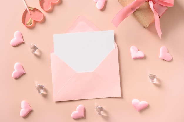 Cartão de saudação de Dia dos Namorados com envelope rosa em branco e pirulitos cor-de-rosa e doces como coração em fundo rosa Vista de cima Espaço de cópia