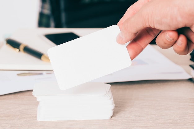 Cartão de visita em branco na mão no fundo da mesa de trabalho embaçada use-nos para mapear informações de contato design templet