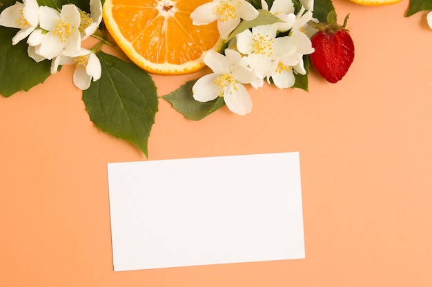 Cartão de visita em branco ou convite e fatias de frutas cítricas e de morango com flores de jasmim no jardim com ...