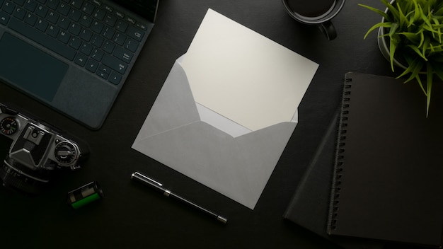 Cartão do convite aberto com envelope cinza na mesa de escritório moderno escuro com material de escritório