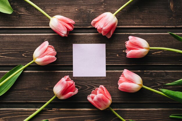 Cartão em branco com tulipas cor de rosa e um adesivo vazio em uma mesa de madeira