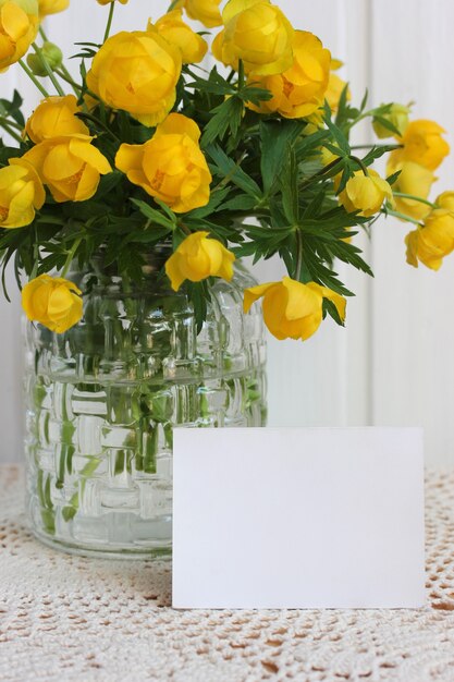 Cartão em branco e flores amarelas da primavera em um vaso de vidro sobre a mesa