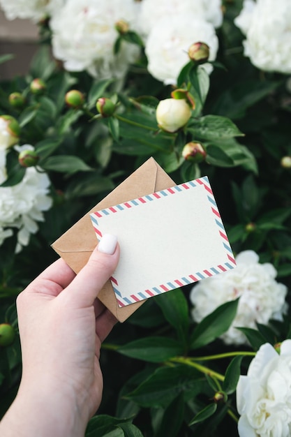 Cartão em branco e um envelope de artesanato na mão de uma mulher no jardim