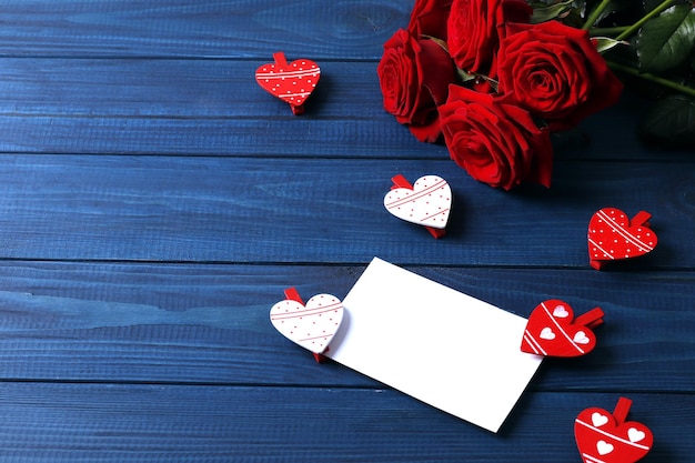 Cartão em branco, rosas vermelhas e decoração de coração em fundo de madeira, vista superior com espaço para texto. Celebração do dia dos namorados