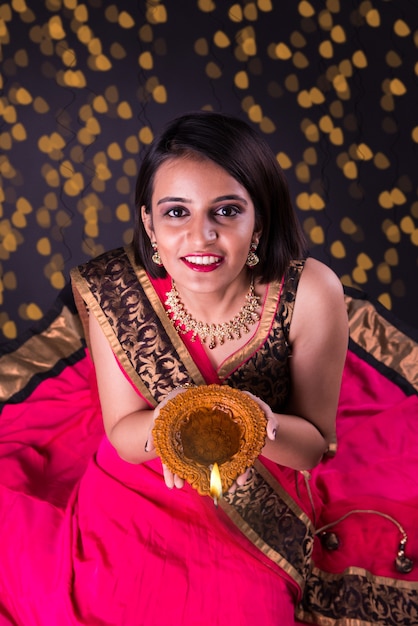 Cartão feliz diwali mostrando uma linda garota indiana segurando uma diya ou lâmpada de óleo de terracota sobre fundo preto