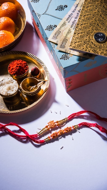 Cartão feliz Raksha Bandhan ou Rakhi usando linha de design, Diya, Pooja Thali, caixa de presente, notas e doces indianos, etc. Iluminação temperamental, foco seletivo
