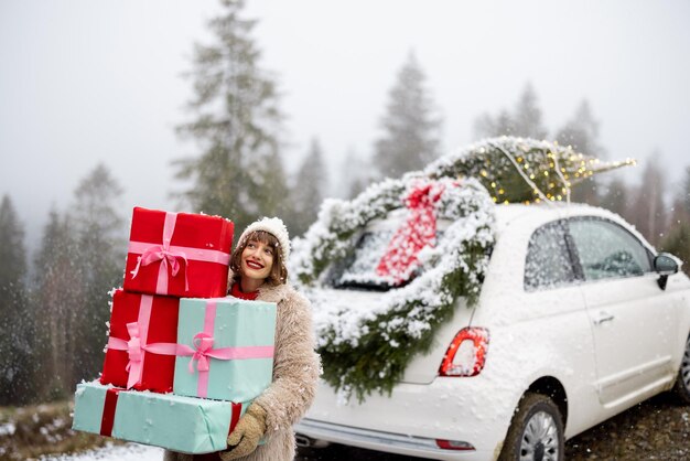 Cartão fotográfico de Natal de uma mulher com presentes e carro nas montanhas em tempo de neve