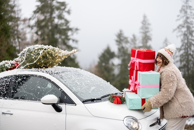 Cartão fotográfico de Natal de uma mulher com presentes e carro nas montanhas em tempo de neve