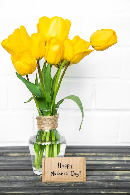 cartão para dia das mães e tulipas amarelas na mesa de madeira