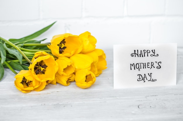 cartão para dia das mães e tulipas amarelas na mesa de madeira