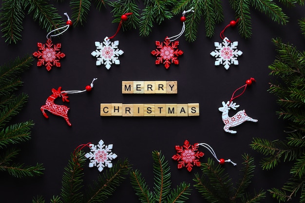 Cartão postal com galhos de árvores de natal, flocos de neve, brinquedos de natal e letras de madeira feliz natal