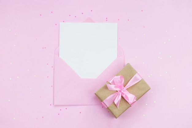 Cartão vazio branco com espaço de cópia em envelope rosa em fundo rosa com caixa de presente
