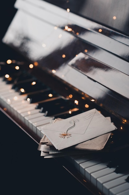 Cartas de correo de caracol de papel en sobres en teclas de piano con flores secas sobre luces navideñas brillantes de cerca Estilo de vida romántico Día de San Valentín