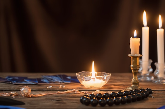 Foto cartas de adivinhação e velas acesas em uma mesa de madeira com fundo marrom escuro