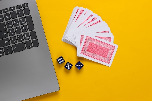 Cartas de jogar e dados azuis, teclado do laptop em fundo amarelo. casino de pôquer online. vista do topo