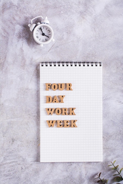 Cartas de madeira do conceito de semana de trabalho de quatro dias no notebook e na parte superior do despertador e na visão vertical