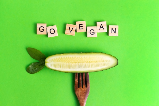 Cartas veganas veganas eco pepino más saludable en un tenedor de madera sobre una superficie verde
