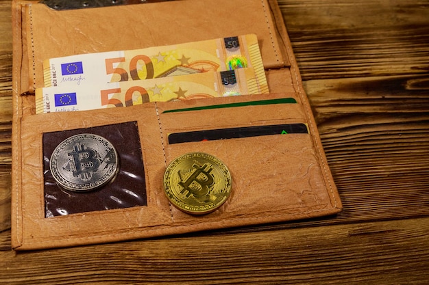 Carteira com notas de cinquenta euros e bitcoins em fundo de madeira