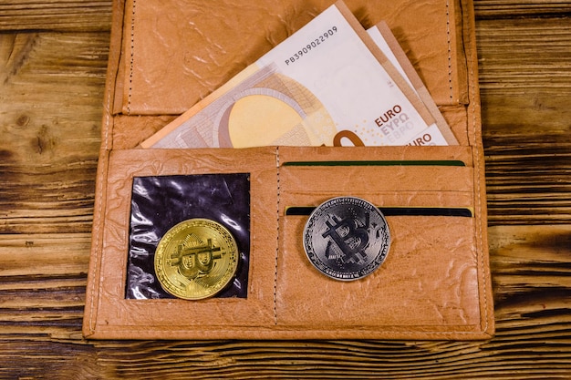 Carteira de couro marrom com notas de cinquenta euros e bitcoins no fundo de madeira