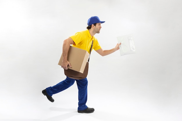 Foto carteiro correndo com um pacote em uma parede branca. copie o espaço.