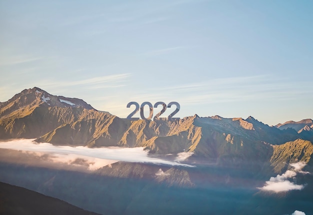 Un cartel de feliz año nuevo 2022 en la cima de la montaña con puesta de sol, símbolo de nuevos éxitos y oportunidades