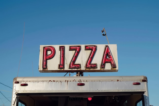 Un cartel iluminado de pizza encima de un camión vendedor de comida callejero