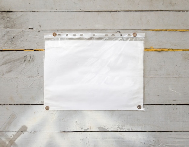 Cartel de papel blanco con remaches, fondo vintage sobre un fondo antiguo de madera gris. Pared con textura de madera, pesa un cartel de cartón en blanco blanco iluminado por el sol, primer plano
