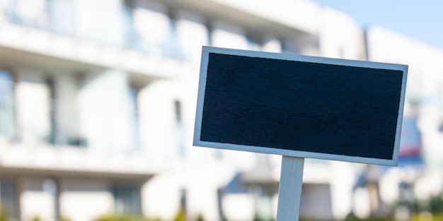 Cartelera negra en blanco contra el nuevo edificio de apartamentos plantilla de maqueta vacía etiqueta de pizarra hogar para