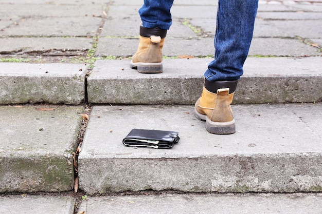 Cartera de cuero perdida y piernas masculinas caminando al aire libre