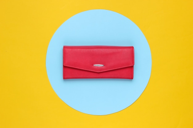 Cartera de mujer elegante de cuero rojo sobre fondo amarillo con círculo azul pastel. Bodegón de moda minimalista creativo. Vista superior