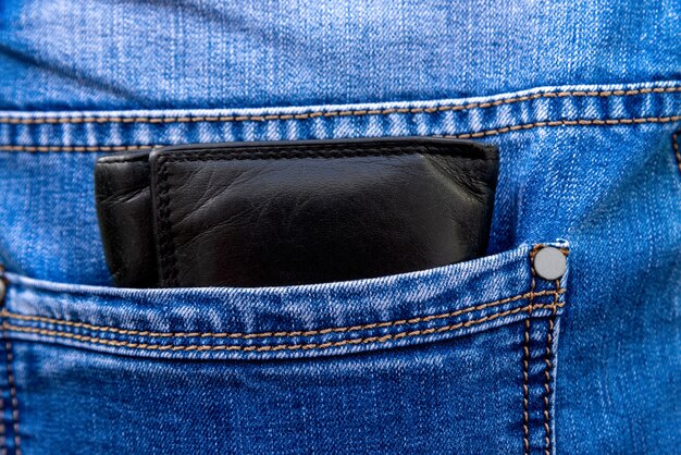 Foto cartera de piel negra en el bolsillo trasero del pantalón. dinero guardado en el bolsillo de los jeans
