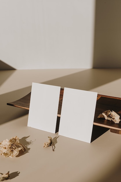 Cartões de folha de papel em branco com espaço de cópia vazio e bandeja de madeira, flores secas com sombras de luz solar em branco