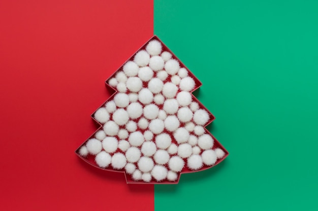 Cartón de árbol de Navidad lleno de bolas de nieve blancas y esponjosas sobre fondo verde y rojo de dos colores.