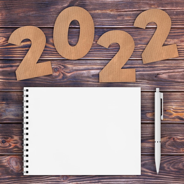 Cartulina números 2022 cartel de feliz año nuevo cerca de cuaderno de tapa de papel espiral blanco con lápiz sobre fondo de mesa de madera. Representación 3D