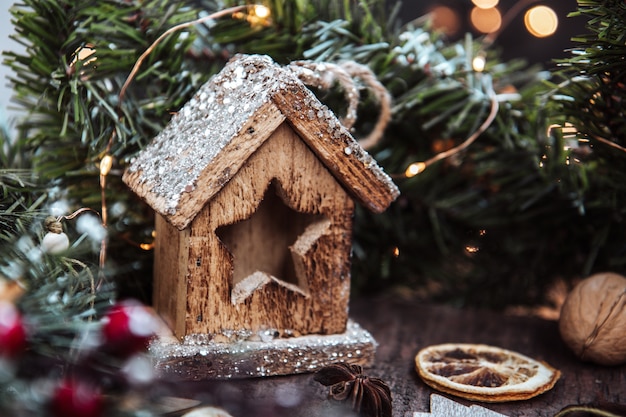 Una casa de Año Nuevo de juguete de madera rodeada por una guirnalda de abeto. Navidad.