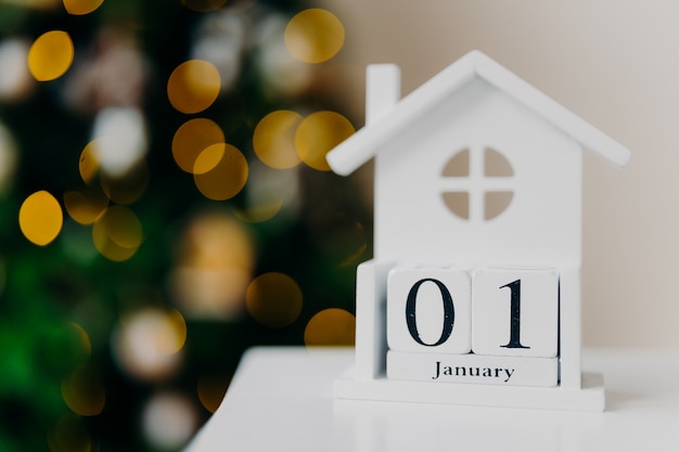 Foto casa blanca creativa con fecha escrita y árbol de navidad con luces. primero de enero. feliz año nuevo, concepto