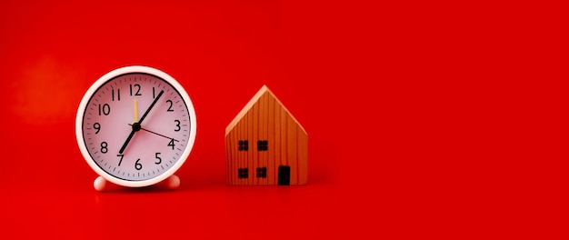 Casa blanca y reloj colocados sobre fondo rojo La idea de tener una casa residencial