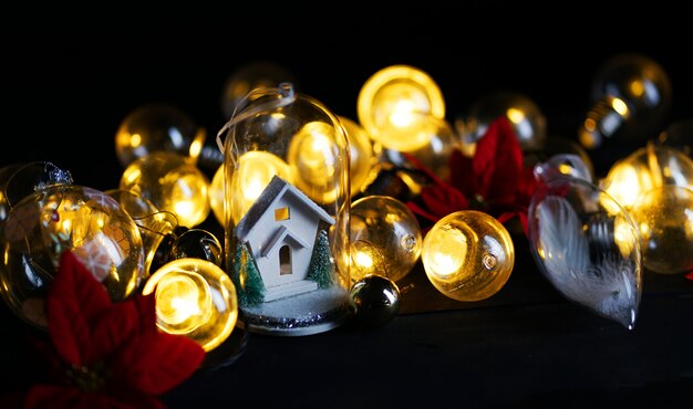 Foto casa branca da decoração do natal dentro do vidro entre o bulbo das luzes e a poinsétia vermelha