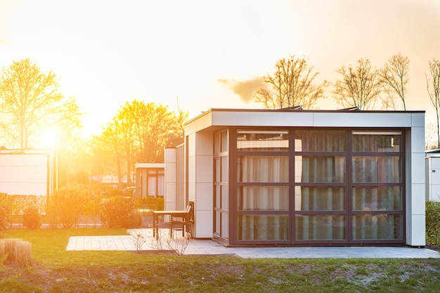 Foto casa de campo moderna con un gran césped y una valla de madera delante de la casa hay una terraza cubierta con una zona de salón en el césped hay árboles y macizos de flores hace sol afuera