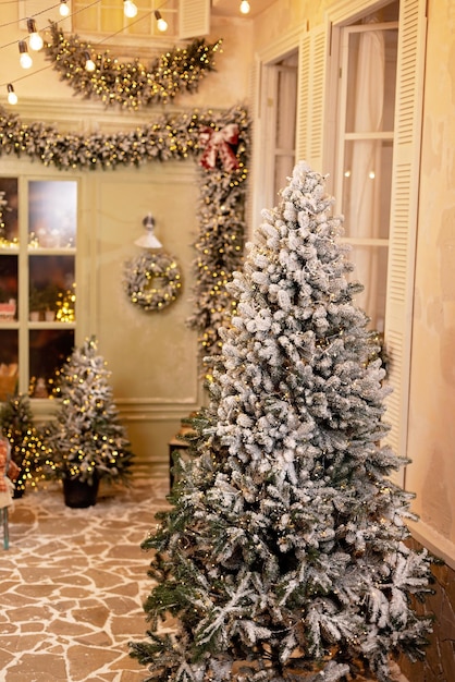 La casa cubierta de nieve está decorada para el nuevo año. Patio de invierno vintage, decorado con adornos de Año Nuevo, árboles de Navidad, linternas de luces. Enfoque selectivo suave.