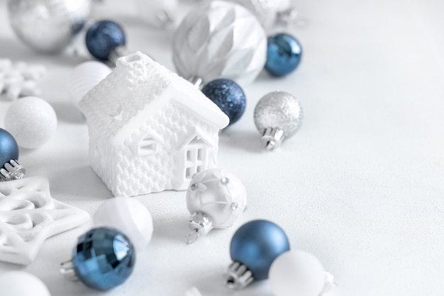 Casa de brinquedo branco com closeup de decorações de natal de azul, branco e prata na mesa branca. composição de inverno monocromática