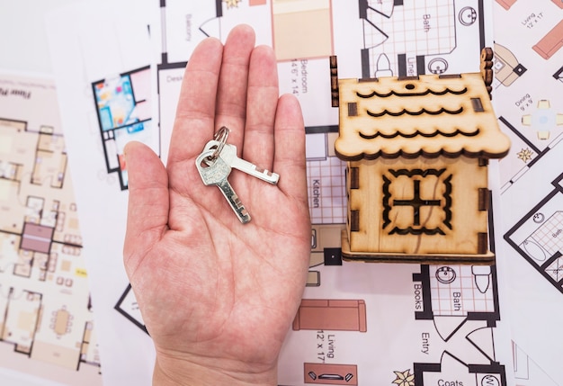 Casa de brinquedo de madeira e chaves na palma da mão. o conceito de renovar, comprar ou construir uma casa.