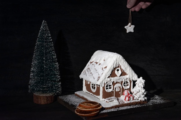 Casa de gengibre ao lado de uma pequena árvore de Natal na composição de Natal de fundo escuro