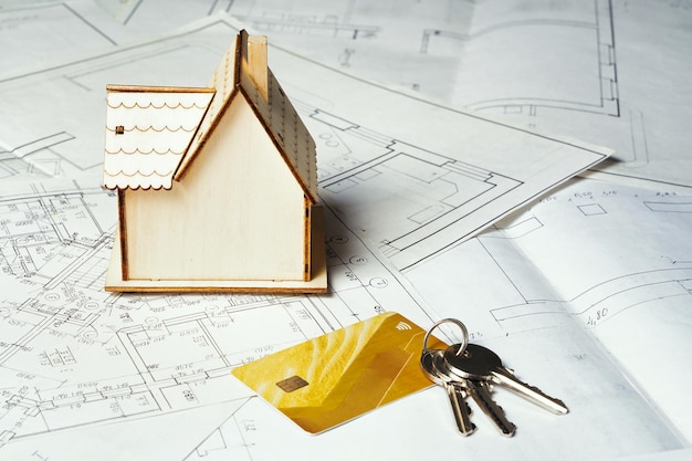 Casa de madeira sobre uma superfície de papel com um projeto e um conceito de molho de chaves construindo uma casa chave na mão p ...