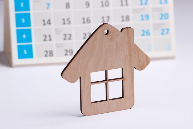 Casa de mini figura com calendário de mesa em fundo branco. Conceito de pagamento de aluguel de habitação