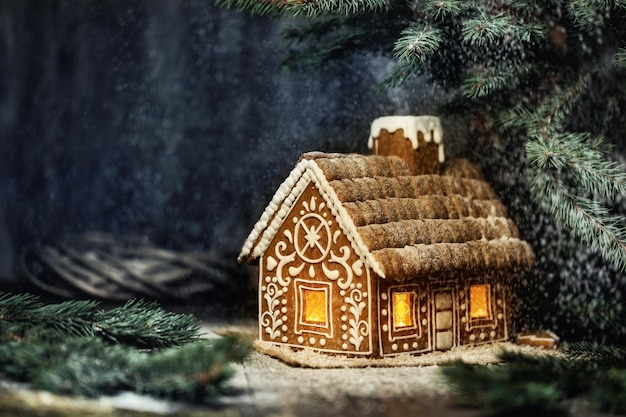 Casa de pão de mel de natal com luzes da janela no inverno nevado forestat noite. design criativo de decoração de alimentos para férias de natal sobre fundo escuro com espaço para cópia